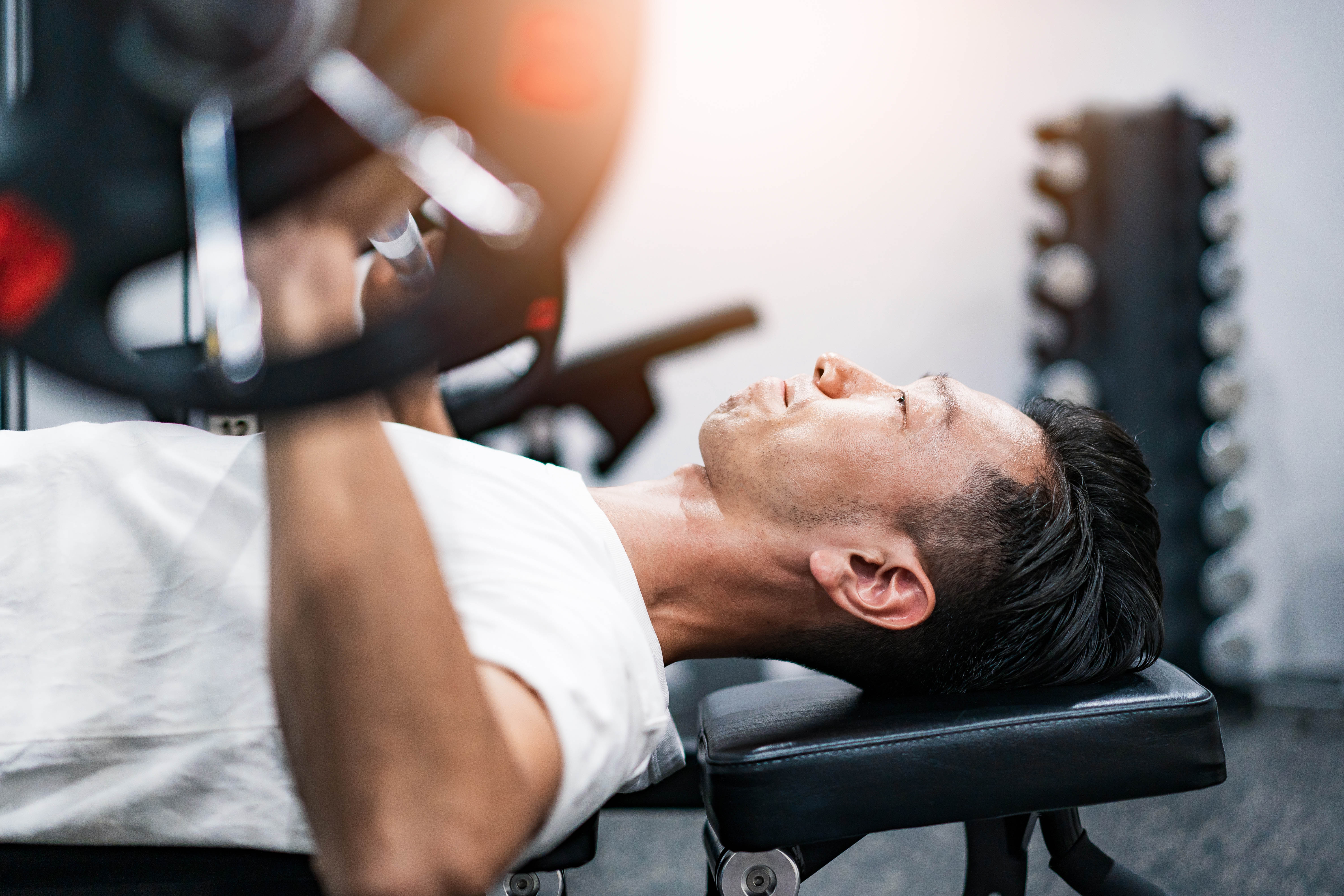 Middle aged Asian man laying on a bench in the gym, preparing to do a chest press